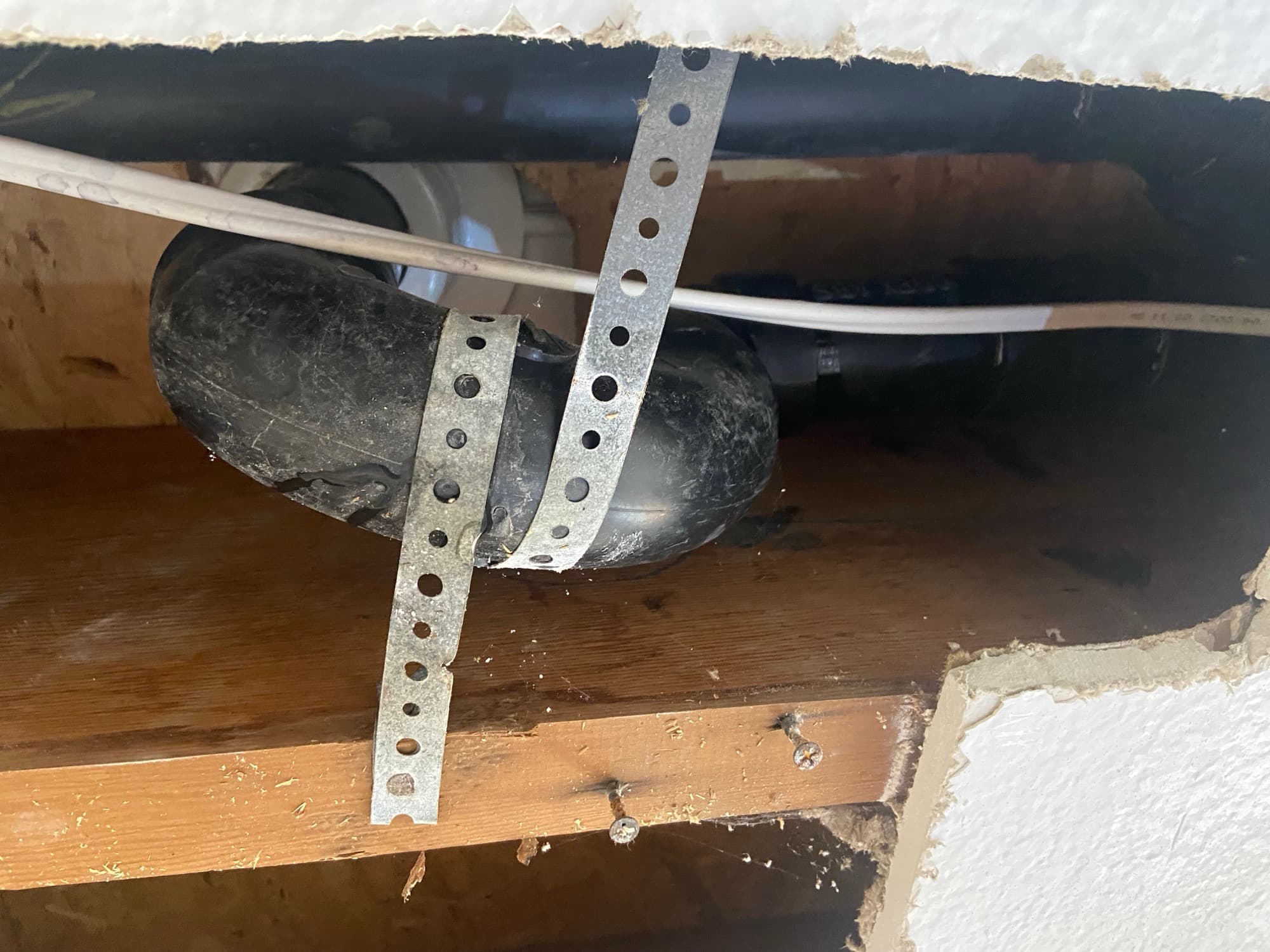 Black ABS drain trap secured with metal pipe straps beneath a sink, Orange County, CA