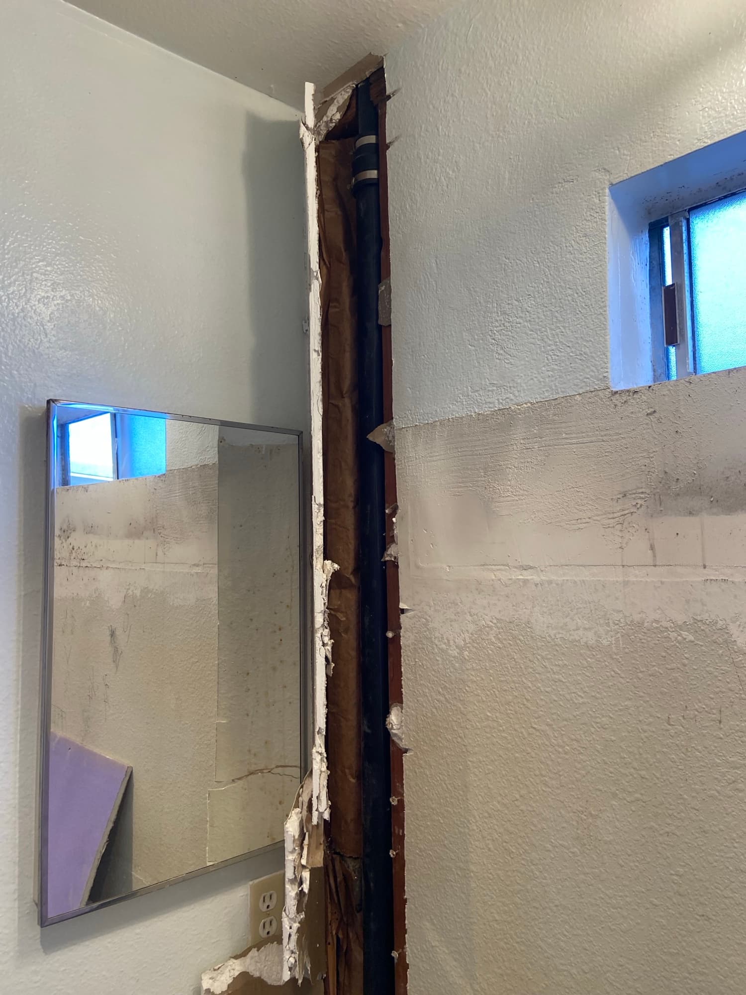 Opened ceiling cavity revealing a black drain pipe above a bathroom mirror, Orange County, CA