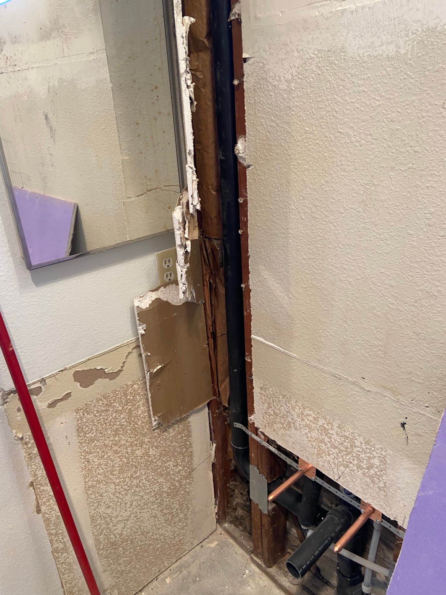 Copper water lines and a black ABS drain pipe exposed behind cut drywall, Orange County, CA