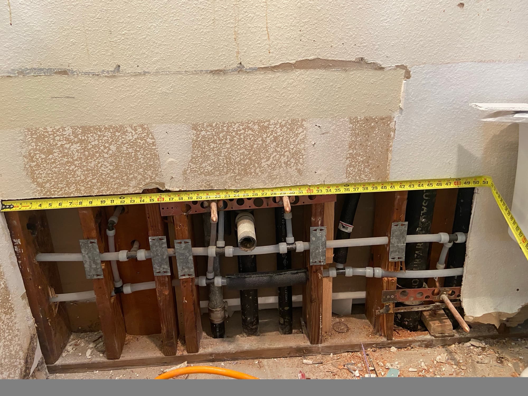 Copper and PEX pipe stubs exposed in a wall stud cavity being measured, Orange County, CA