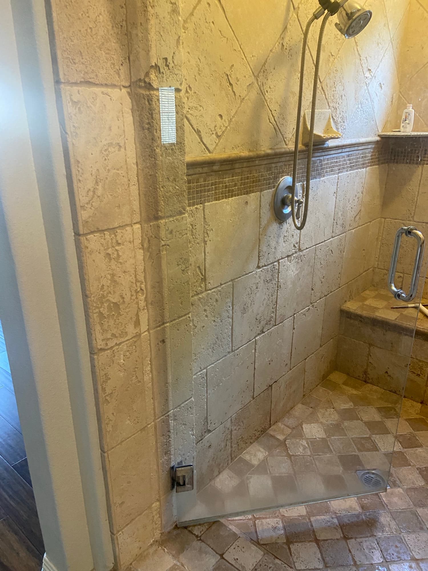 Curbless travertine shower featuring a trench drain and handheld shower wand in Orange County