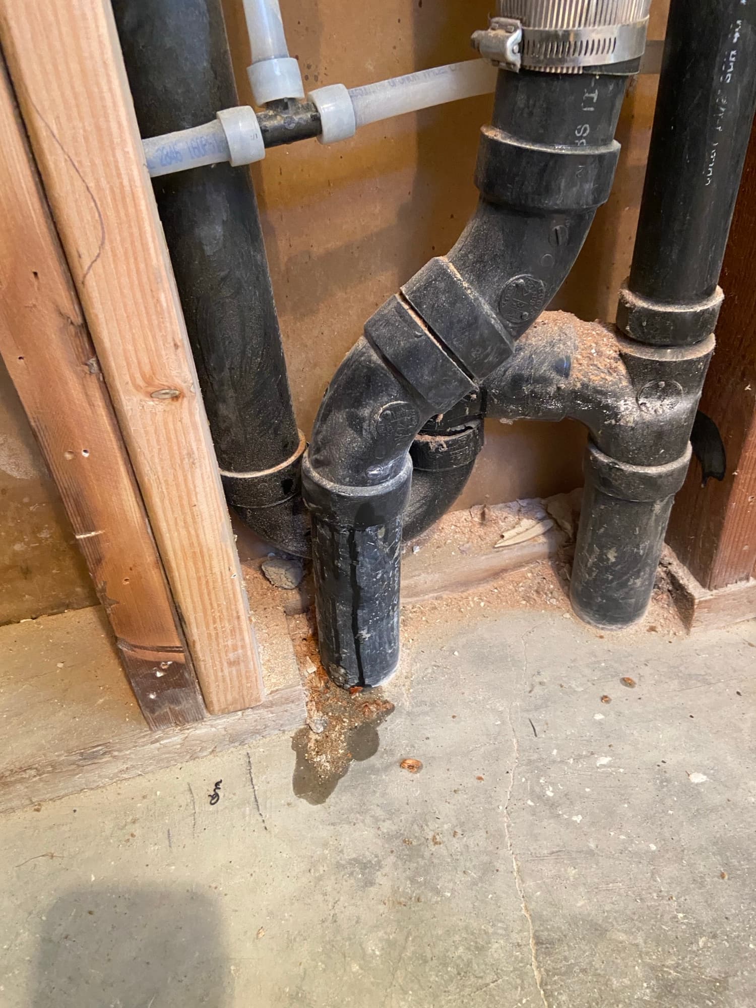 Close-up of ABS drain pipe elbow fittings near a repaired concrete slab, Orange County, CA