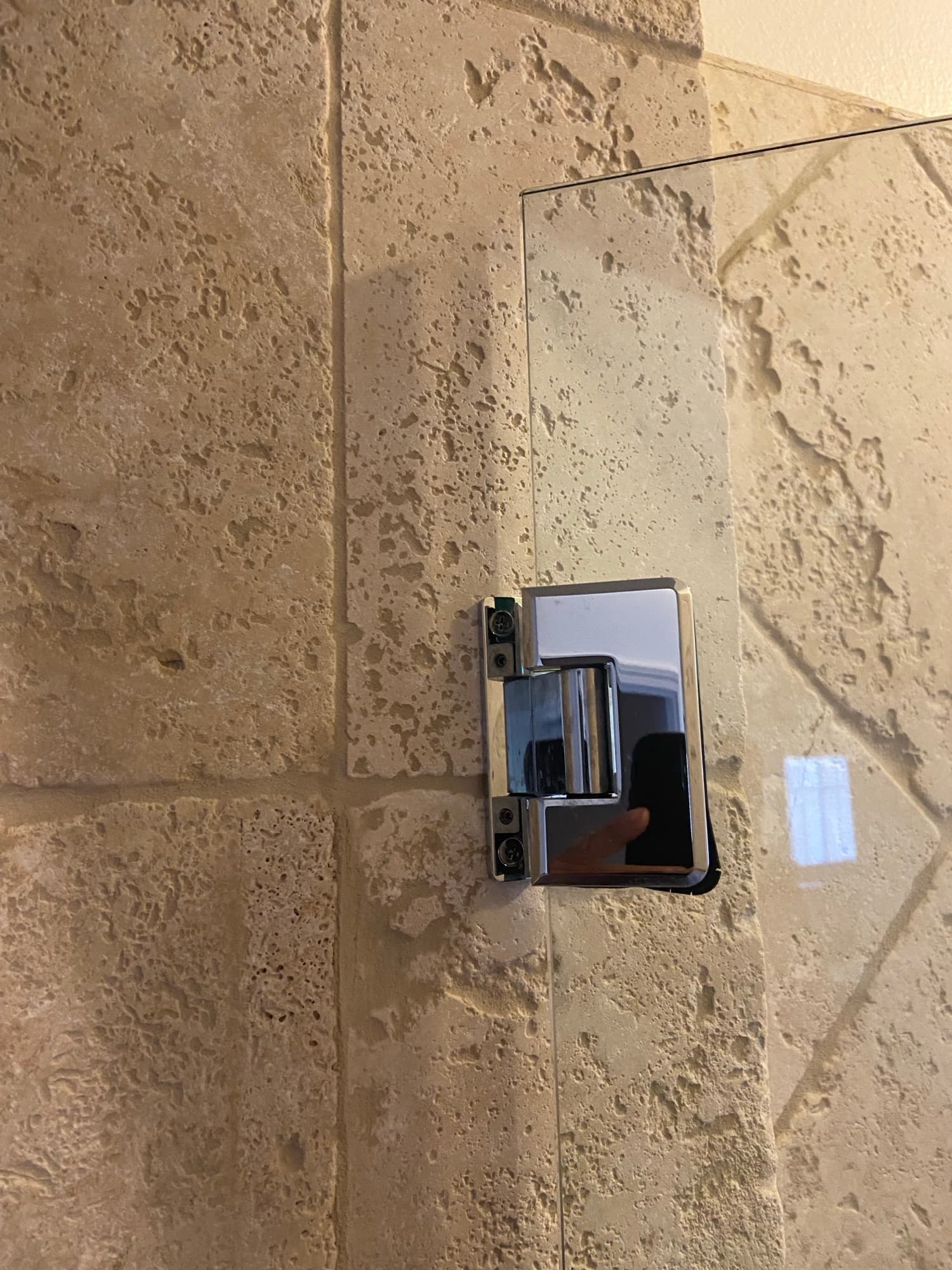 Chrome glass shower door hinge mounted on travertine tile in an Orange County bathroom