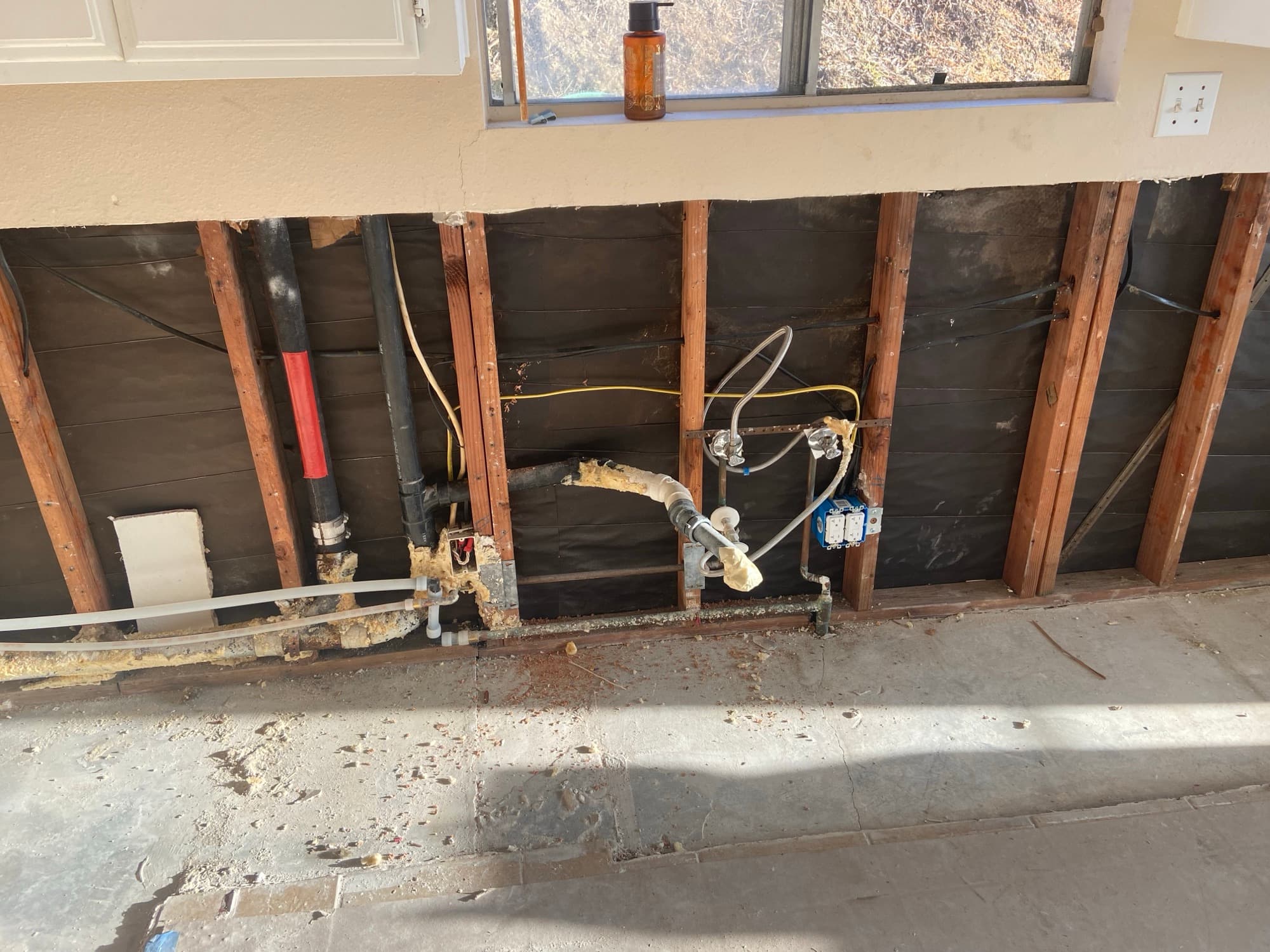 Kitchen wall opened up to expose black drain pipe and PEX supply lines, Orange County, CA