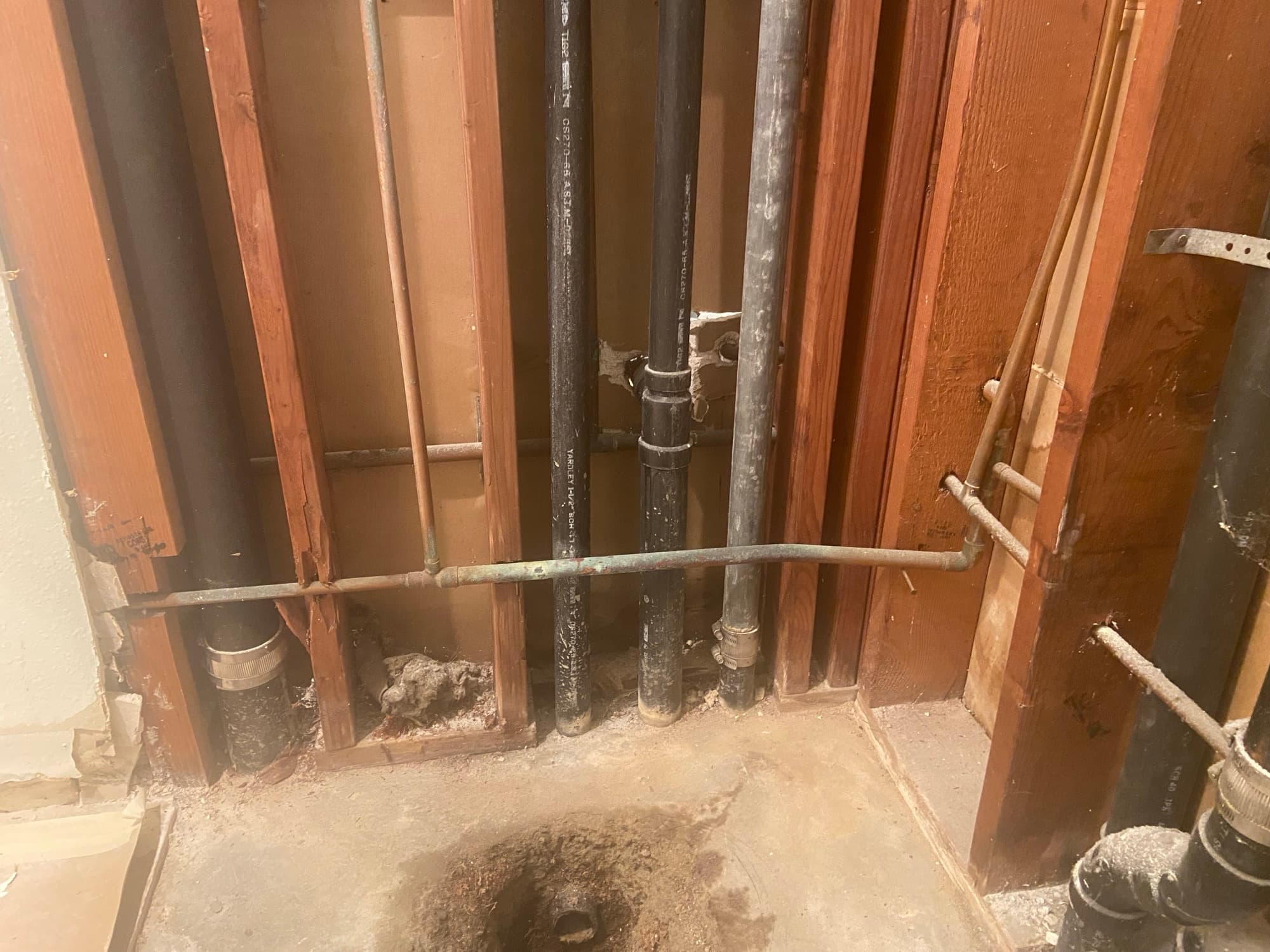 Open wall cavity showing black ABS pipe and copper line connections during a repipe