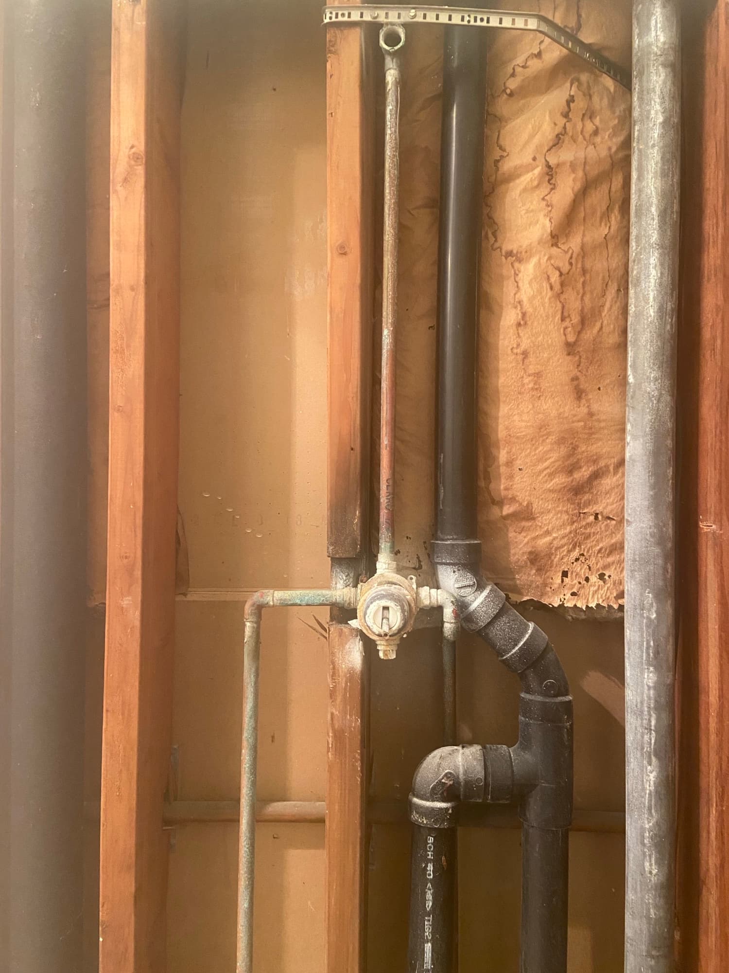 Black pipe elbow fitting connected to a copper line and shutoff valve in a crawlspace