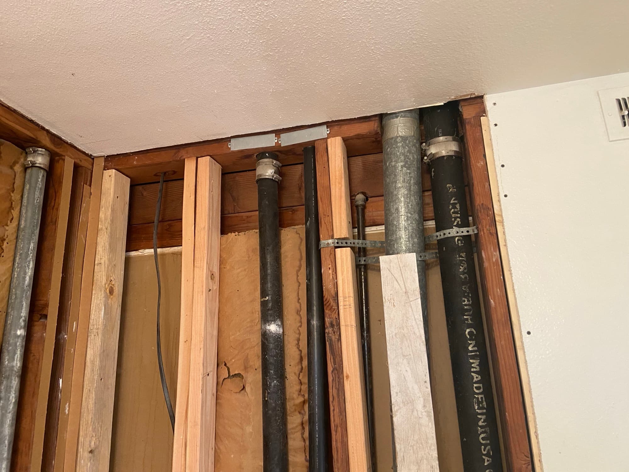 Black ABS vent pipe and galvanized pipe running through ceiling framing, Orange County, CA